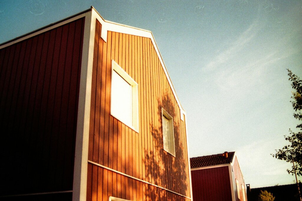 A low-angle shot of vibrant red wooden houses under a clear blue sky, capturing a modern village setting.